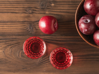 Two glasses of plum alcohol and a bowl of plums on a wooden table. Flat lay.