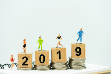 Wall Mural - Miniature people running on a wooden box with number 2019 and coins.