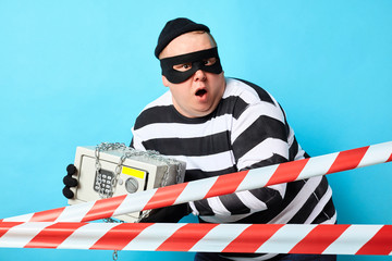 surprised scared burglar trying to hide safe from policemen. isolated blue background, studio shot