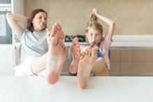 Cute Girl And Her Mother Are Smiling While Eating Ice Cream In The Kitchen With Legs On A Table