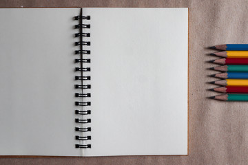 Multi-colored pencils with brown note book on brown paper background