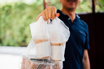 Close-up of male food delivery man on service job giving foods of bubble tea, coffee, lunch box at home