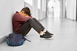 © serhiibobyk - Sad school boy sitting alone on floor at corridor.