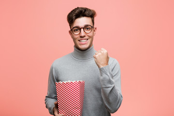 Wall Mural - Young intellectual man holding a popcorn bucket celebrating a victory or success