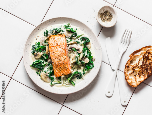 Fotografía Roasted salmon with creamy spinach mushrooms sauce on a light background, top view