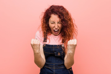 Young pretty ginger redhead woman wearing a jeans dungaree cheering carefree and excited. Victory concept.