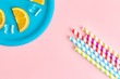 Orangeade abstract made of colorful drinking straws and orange fruit slices with ce cubes on plate isolated on rose.