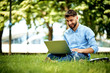 © baranq - Portrait of young businessman sitting in the park and working on laptop