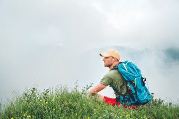 Wall Mural - tired hiker with backpack man resting and enjoying cloudy valley bottom walking by the foggy cloudy 