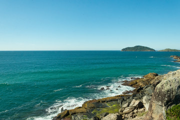 Vista do alto de um rochedo para o mar e uma ilha deserta florestada ao horizonte.