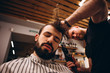 © Ananass - Barbershop. Close-up of man haircut, master does the hair styling in barber shop. Strong muscular bearded barber cuts long black hair of the client