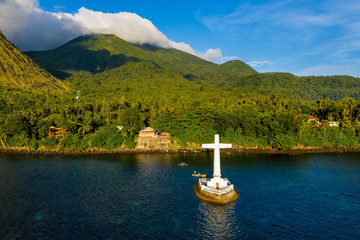 Wall Mural - Aerial drone view of a cross in the ocean with steep Mount Vulcan and Mount Hibok-Hibok behind (Sunken Cemetery, Camiguin, Philippines)