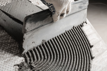 Worker spreading concrete on ceramic tile with spatula, closeup