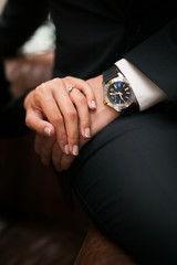 Concept of wrist watch advertising. Close up of holding hands. Elegant man in a black suit and Rich woman in black dress. Young  Fashion stylish man and woman in loft design interior.