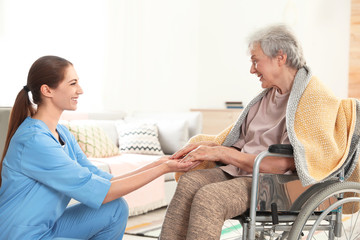 Poster - Nurse holding elderly woman's hands indoors. Assisting senior people