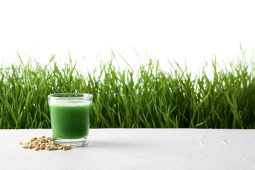 Glass of juice with grains on table and fresh wheat grass against white background. Space for text