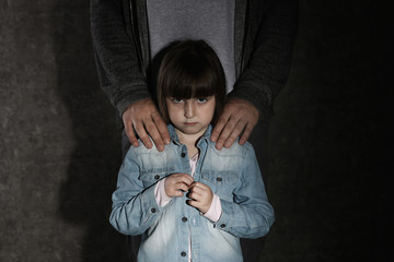 Scared little girl and adult man on dark background. Child in danger