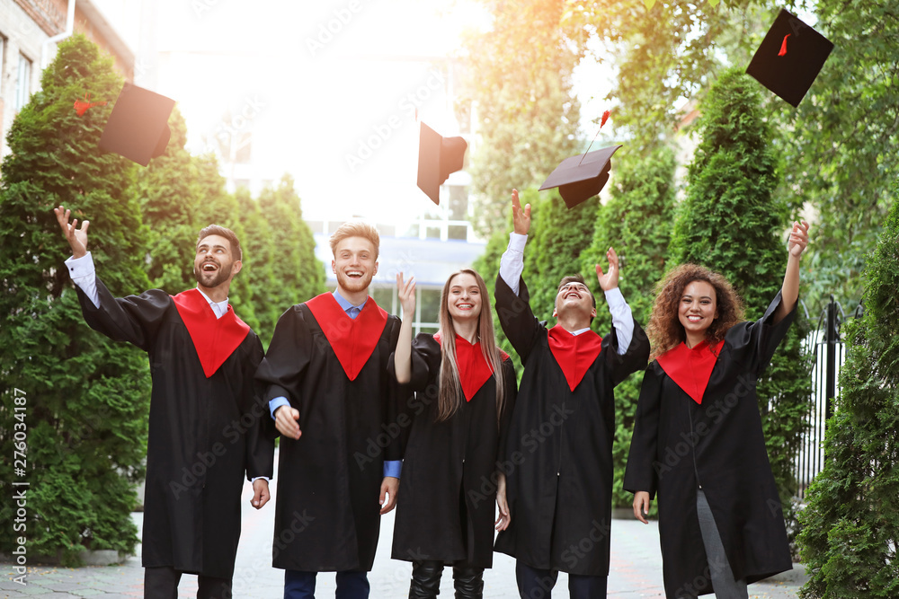 Happy students in bachelor robes throwing hats outdoors