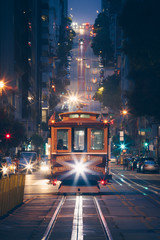 Fototapete - Classic view of historic traditional Cable Cars riding on famous California Street at night with city lights, San Francisco, California, USA