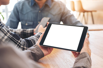 A woman using and looking at mockup tablet pc on wooden table with friends in background