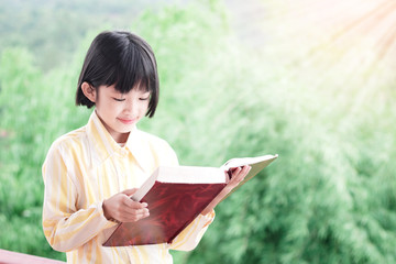 Poster - Cute little girl reading book green nature background