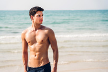Portrait Of Smiling Handsome Sexy Man Showing Muscular Fit Body Standing On The Tropical Beach.Summer Vacations