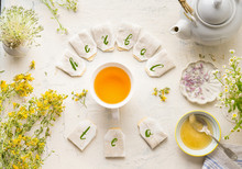 White Cup With Frame Of Tea Bags And Text Herbal Tea On White Table Background, Top View. Herbal Tea Set With Teapot , Honey And Fresh Medical Herbs And Flowers. Healthy Preventive Drink Treatment