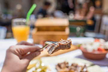 Sliced grilled lamb chops on a fork. Woman have a dinner in a greek tavern