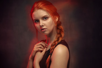 Beauty portrait of redhead girl with long braid and crossed hands. Magical glow of red light around the model