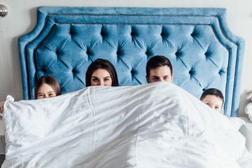 Happy family lying under blanket in bed at home , time together..