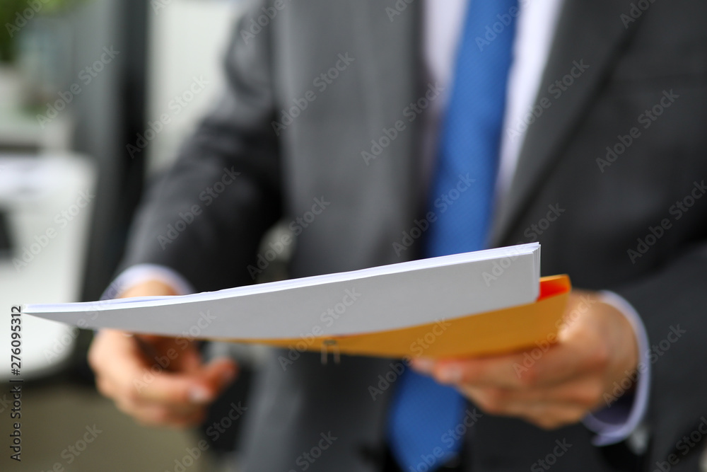Clerk hand in suit and tie holding yellow envelope containing batch of important papers - obrazy, fototapety, plakaty 