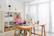 © DragonImages - Relaxed smiling aged woman sitting at her table in office of creative studio