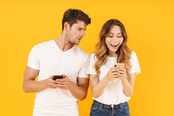 Canvas Print - Photo of young couple man and woman in basic t-shirts holding and peeking at cell phones