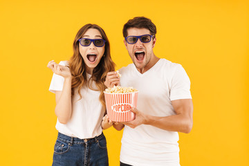 Portrait of delighted couple man and woman in 3D glasses rejoicing while standing together with popcorn bucket