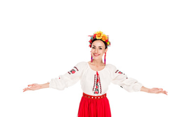 Wall Mural - happy brunette young woman in national Ukrainian costume doing welcome gesture isolated on white