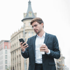 Young businessman using smartphone holding coffee cup in hand