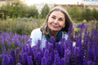 © shurkin_son - Summertime, people and lifestyle concept. Gorgeous happy cheerful middle aged female with gray hair sitting outdoors among many beautiful violet flowers, having joyful facial expression, smiling
