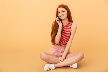 Sticker - Cheerful young beautiful redhead woman posing isolated over yellow background talking by mobile phone.