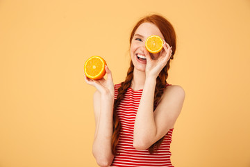 Poster - Happy  young beautiful redhead woman posing isolated over yellow background holding orange.