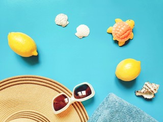 Wall Mural - Summer travel mockup and banner. Women's sun beach hat, lemons, towel, seashells and rubber toy turtle on a blue background. Flat lay composition photography, top view picture