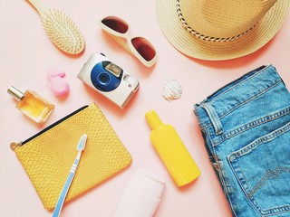 Wall Mural - Summer trip stuff, girly travel items on a pink background. Cosmetic bag, perfume, yellow sunscreen bottle, shampoo, toothbrush, hair brush, sunglasses, camera, sun hat and jeans. Flat lay photo