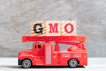 Wall Mural - Red fire truck hold letter block in word GMO (abbreviation of Genetically Modified Organisms) on wood background