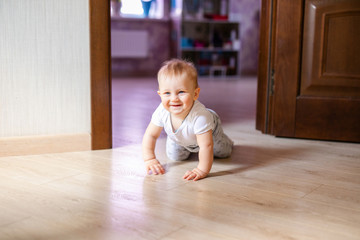 Cute little baby boy lying on hardwood and smiling. Child crawling over wooden parquet and looking up with happy face. View from above. Copyspace