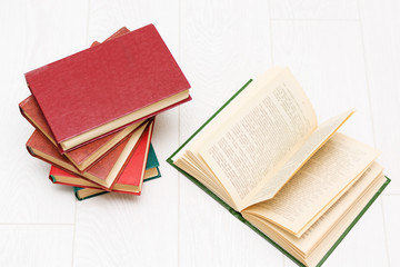 stack of books lies on a white wooden table, one book is opened, with text.