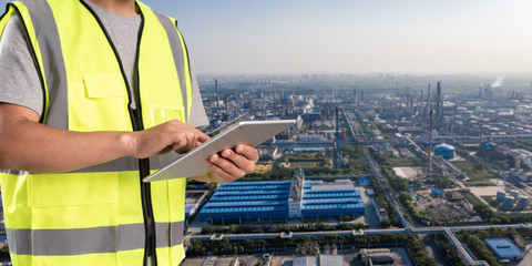 Canvas Print - worker working on pad with oil and gas refinery background,Smart factory concept.