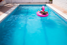 Young Man Floating In A Inflatable Flamingo In A Blue Pool A Sunny Day Of Summer Vacation	