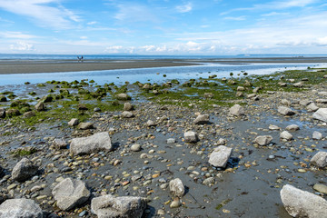 sandy beach by the ocean at low tide with rocks filled edge and cloud on the blue sky above the horizon