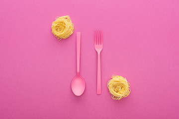 Wall Mural - pink plastic fork and spoon upside down near vermicelli pasta on pink background