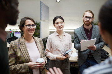 Waist up portrait of multi-ethnic group of business people listening to colleague and taking notes while discussing project in office