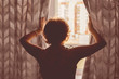 © Mihail - adult woman opens the window curtains looking forward the future day